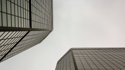 Two modern glass skyscrapers with angular perspectives, seen from below, against a cloudy sky